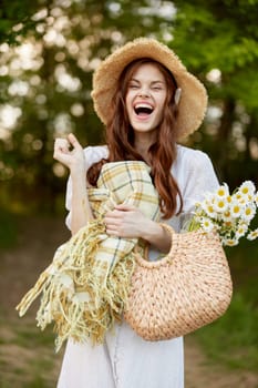 joyful woman in a wicker hat and with a basket in her hands stands in nature