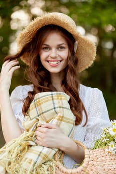 joyful woman in a wicker hat and with a basket in her hands stands in nature