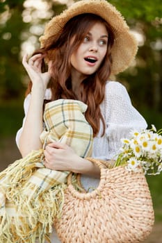 joyful woman in a wicker hat and with a basket in her hands stands in nature