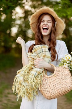 joyful woman in a wicker hat and with a basket in her hands stands in nature