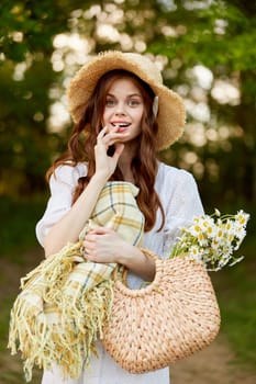 joyful woman in a wicker hat and with a basket in her hands stands in nature