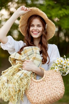 joyful woman in a wicker hat and with a basket in her hands stands in nature