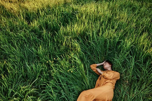 a sweet, calm woman in an orange dress lies in a green field enjoying the silence and peace. Horizontal photo taken from above. High quality photo