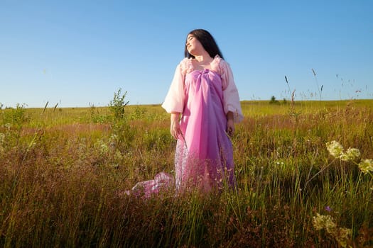 Young plump curvy beautiful teenage girl in a field or meadow on sunny summer day in the evening sunset sun. Plump black-haired and black-eyed oriental model from the east fairy tale