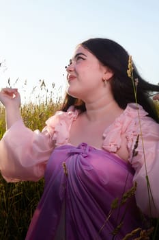 Young plump curvy beautiful teenage girl in a field or meadow on sunny summer day in the evening sunset sun. Plump black-haired and black-eyed oriental model from the east fairy tale