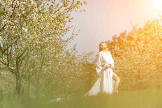 Blond blooming garden. A woman in a white dress walks through a blossoming cherry orchard. Long dress flies to the sides