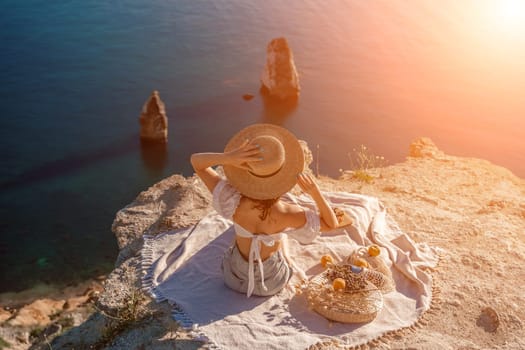 woman sea travel. photo of a beautiful woman with long blond hair in a pink shirt and denim shorts and a hat having a picnic on a hill overlooking the sea.