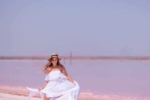 Woman in pink salt lake. She in a white dress and hat enjoys the scenic view of a pink salt lake as she walks along the white, salty shore, creating a lasting memory