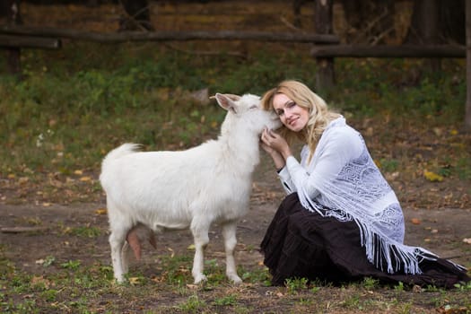 Sweet woman stroking white goats on a green glade