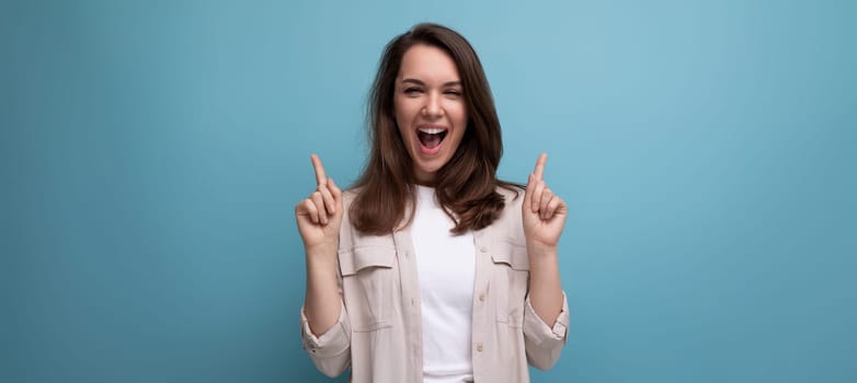 ecstatic 30s dark haired woman in beige shirt on blue background.