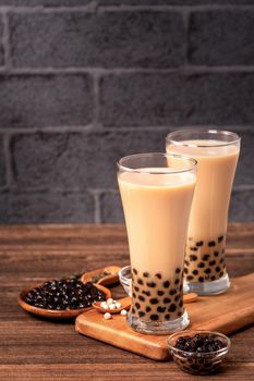 Delicious bubble milk tea with tapioca pearl ball in glass on wooden table and dark gray brick background, popular food and drink in Taiwan, close up
