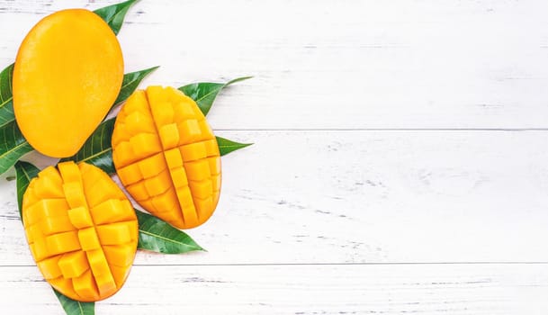 Beautiful chopped mango with green leaves on bright white color timber background. Above Top view, flat lay, copy space, close up. Tropical fruit concept.