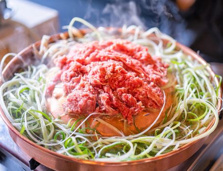 Beef barbecue bulgogi in Korean restaurant in Seoul, lifestyle fresh korean food cuisine on copper pan with sliced green onion, close up, copy space