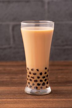 Delicious bubble milk tea with tapioca pearl ball in glass on wooden table and dark gray brick background, popular food and drink in Taiwan, close up