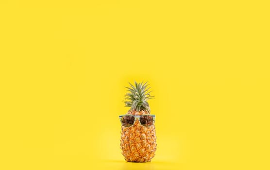 Creative pineapple looking up with sunglasses and shell isolated on yellow background, summer vacation beach idea design pattern, copy space close up