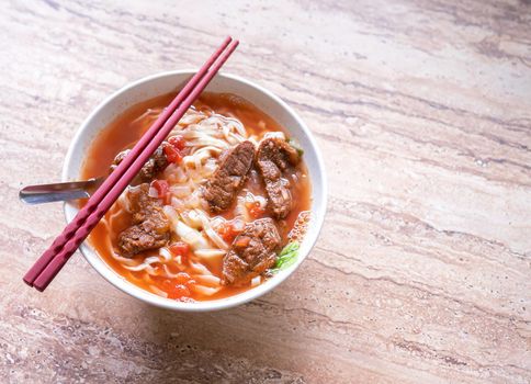 Beef noodle ramen meal with tomato sauce broth in bowl on bright wooden table, famous chinese style food in Taiwan, close up, top view, copy space