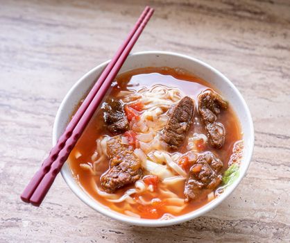 Beef noodle ramen meal with tomato sauce broth in bowl on bright wooden table, famous chinese style food in Taiwan, close up, top view, copy space