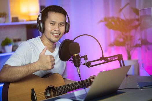 Man singing with headphone and playing guitar recording new song with microphone in the home recording studio