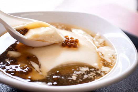 Popular Taiwan gourmet - Dessert of tapioca pearl ball (bubble) mixed bean curd tofu pudding (douhua, dou hua) in white bowl, close up, lifestyle