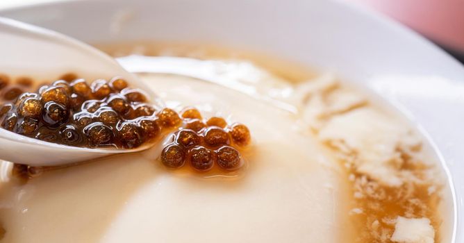 Popular Taiwan gourmet - Dessert of tapioca pearl ball (bubble) mixed bean curd tofu pudding (douhua, dou hua) in white bowl, close up, lifestyle