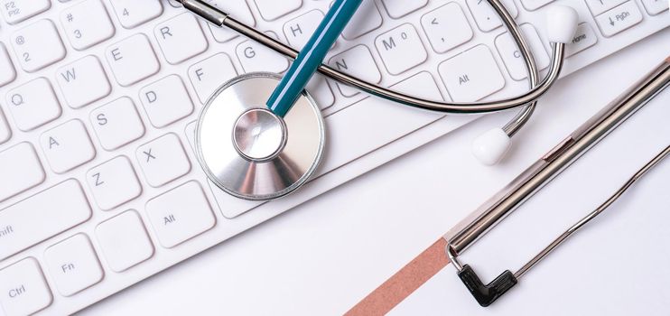 Stethoscope on keyboard on white table background. Online medical information treatment technology office concept, top view, flat lay, copy space