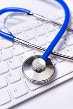 Blue stethoscope on computer keyboard on white table background. Online medical information treatment technology concept, close up, macro, copy space