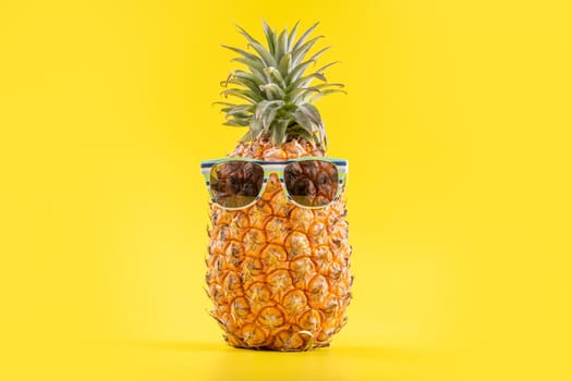 Creative pineapple looking up with sunglasses and shell isolated on yellow background, summer vacation beach idea design pattern, copy space close up