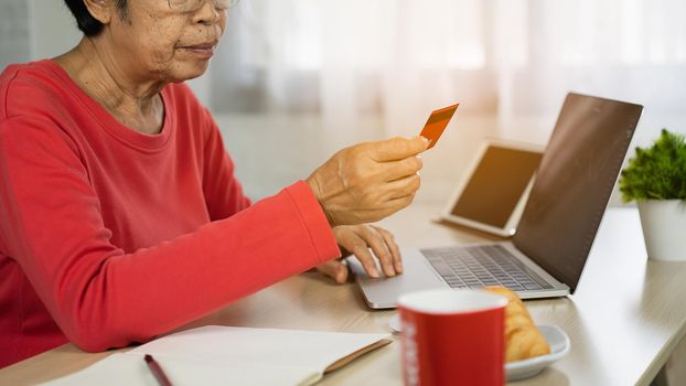 senior women looking for credit card and using laptop shopping online