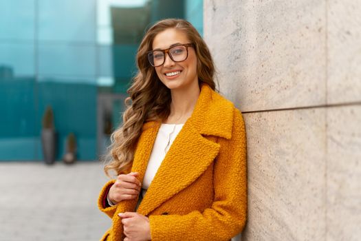 Business woman dressed yellow coat standing outdoors corporative building background Caucasian female business person eyeglasses on city street near office building with windows Stylish businesswoman