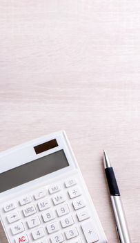 White calculator and pen on bright wooden table, analytics and statistics of financial profit, investment risk concept, copy space, top view flat lay