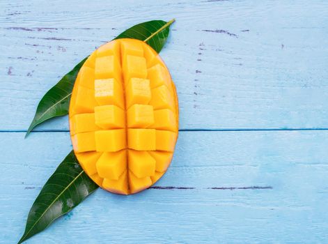 Fresh chopped mango with green leaves on bright blue color timber background. Above Top view, flat lay, copy space, close up. Tropical fruit concept.