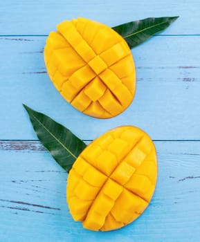 Fresh chopped mango with green leaves on bright blue color timber background. Above Top view, flat lay, copy space, close up. Tropical fruit concept.