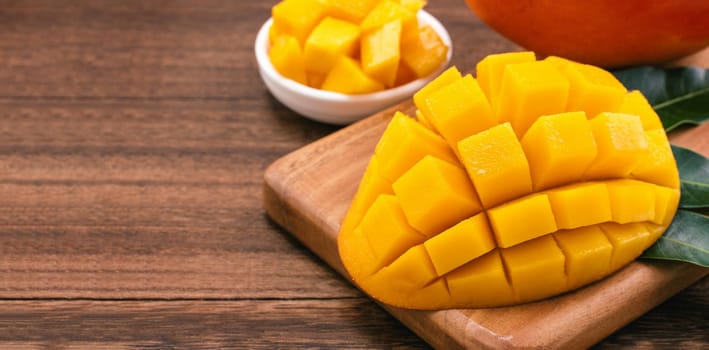 Fresh chopped mango cubes on wooden cutting board and rustic timber background. Tropical summer fruit concept, close up, macro, copy space. 