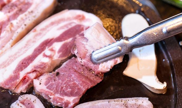 Pan-fried black pork meal in Korea restaurant, fresh delicious korean food cuisine on iron plate with lettuce, close up, copy space, lifestyle