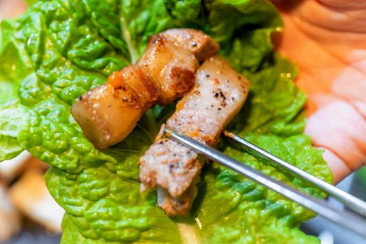 Pan-fried cooked black pork meal in Korea restaurant, fresh delicious korean food cuisine on iron plate with lettuce, close up, copy space, lifestyle