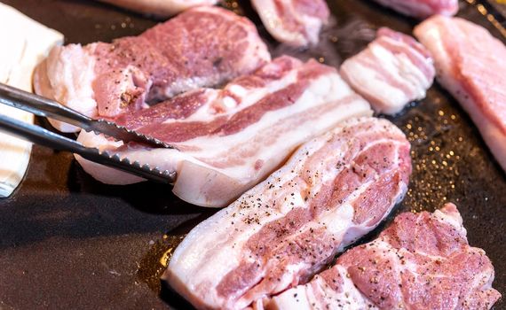 Pan-fried black pork meal in Korea restaurant, fresh delicious korean food cuisine on iron plate with lettuce, close up, copy space, lifestyle