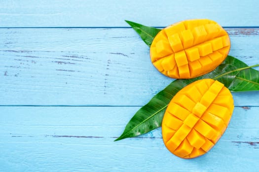 Fresh chopped mango with green leaves on bright blue color timber background. Above Top view, flat lay, copy space, close up. Tropical fruit concept.