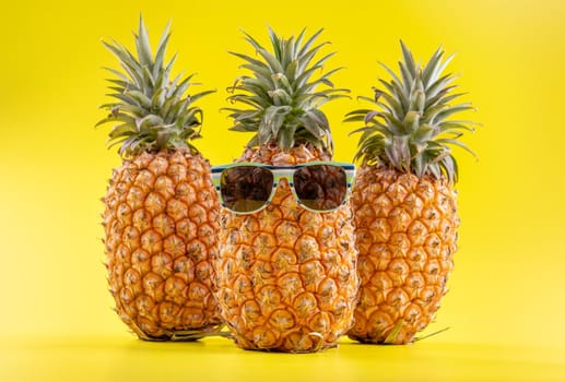 Creative pineapple looking up with sunglasses and shell isolated on yellow background, summer vacation beach idea design pattern, copy space close up