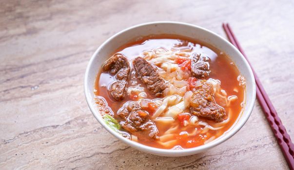 Beef noodle ramen meal with tomato sauce broth in bowl on bright wooden table, famous chinese style food in Taiwan, close up, top view, copy space