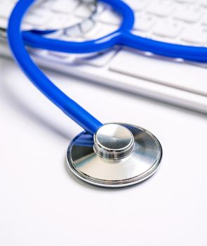 Blue stethoscope on computer keyboard on white table background. Online medical information treatment technology concept, close up, macro, copy space