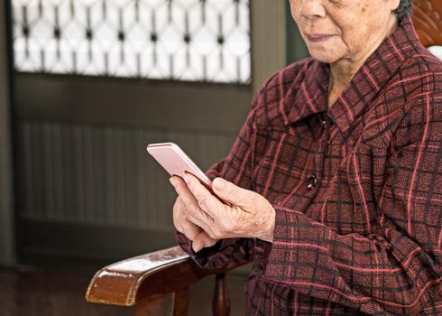 Asian elderly woman sitting and looking through something on modern smartphone, making connection with others at home, living technology, close up
