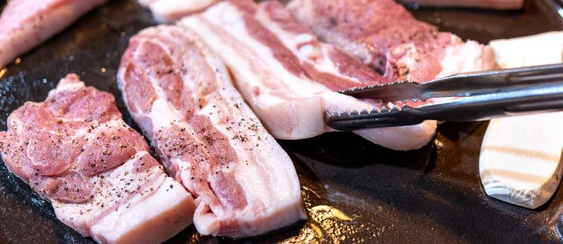 Pan-fried black pork meal in Korea restaurant, fresh delicious korean food cuisine on iron plate with lettuce, close up, copy space, lifestyle