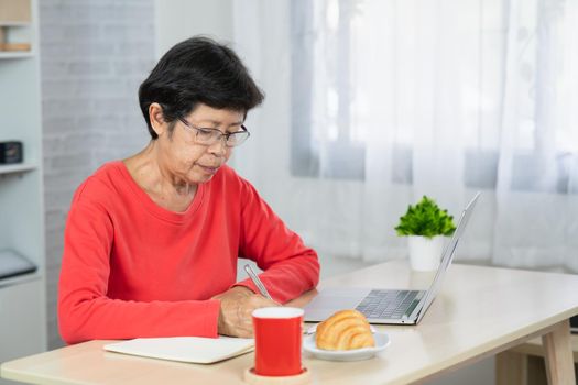 Senior asian woman relaxing using laptop computer while sitting on table.