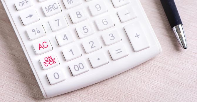 White calculator and pen on bright wooden table, analytics and statistics of financial profit, investment risk concept, copy space, macro, close up