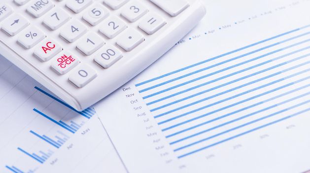 White calculator and report with chart and graph, concept of annual financial profit overview, banking and investment, copy space, macro, close up