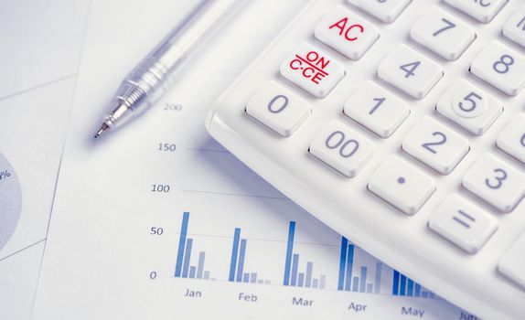 White calculator and report with chart and graph, concept of annual financial profit overview, banking and investment, close up, copy space, macro