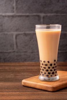 Delicious bubble milk tea with tapioca pearl ball in glass on wooden table and dark gray brick background, popular food and drink in Taiwan, close up