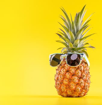 Creative pineapple looking up with sunglasses and shell isolated on yellow background, summer vacation beach idea design pattern, copy space close up