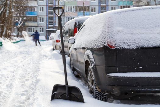 plastic snow shovel in front of snow-covered car at sunny winter morning with man, shoveling in blurry background