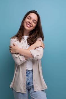 romantic dreaming european young brunette woman in shirt and jeans on blue background.